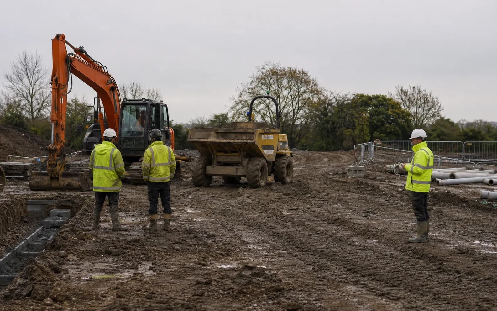 Idle excavator, dumper and site operatives during a construction delay.